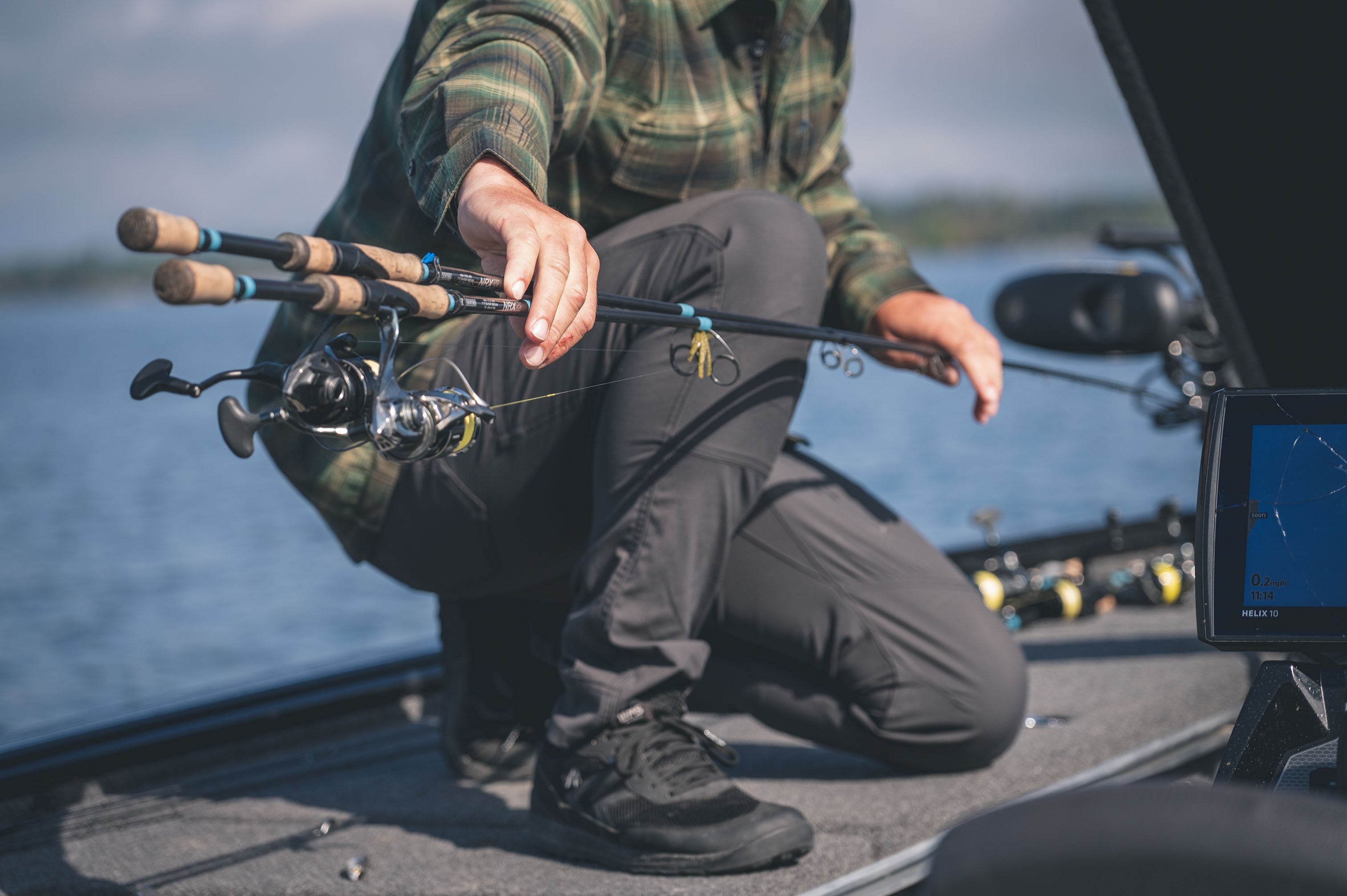 Angler kneeling on a fishing boat deck while setting up multiple fishing rods and reels on a calm lake